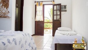 Una habitación con una cama, una mesita con un cojín, aire acondicionado de pared y una puerta que da al exterior.