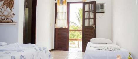 Una habitación con una cama, una mesita con un cojín, aire acondicionado de pared y una puerta que da al exterior.