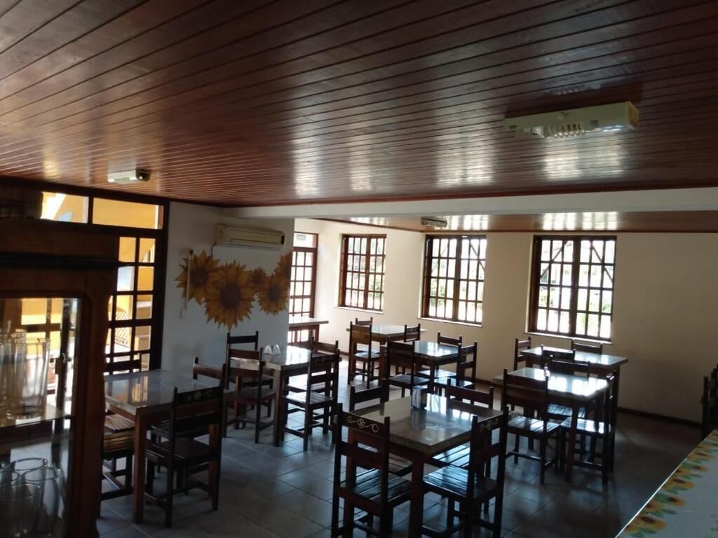 A spacious dining area with wooden tables and chairs, large windows allowing natural light, and a ceiling with wooden panels.