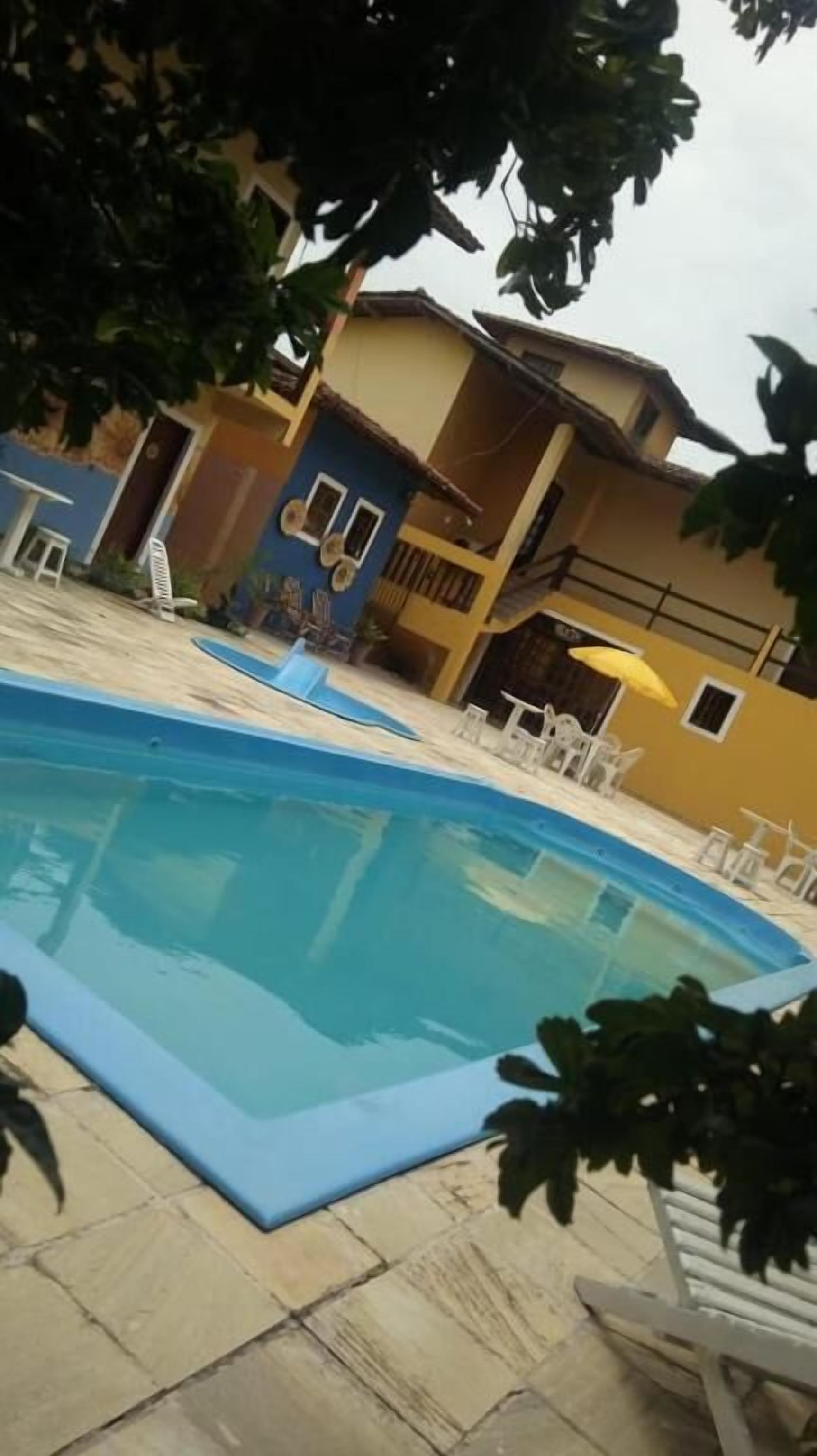 A swimming pool with a tiled deck, surrounded by outdoor furniture and a building with multiple windows and balconies.