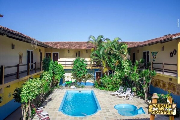 A courtyard with a swimming pool, lounge chairs, and lush greenery.