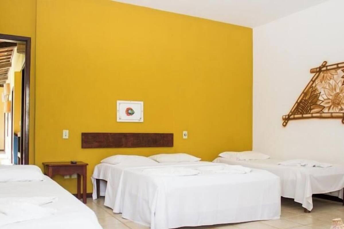 A hotel room with three beds, a wooden headboard, a wall-mounted artwork, and a small table.