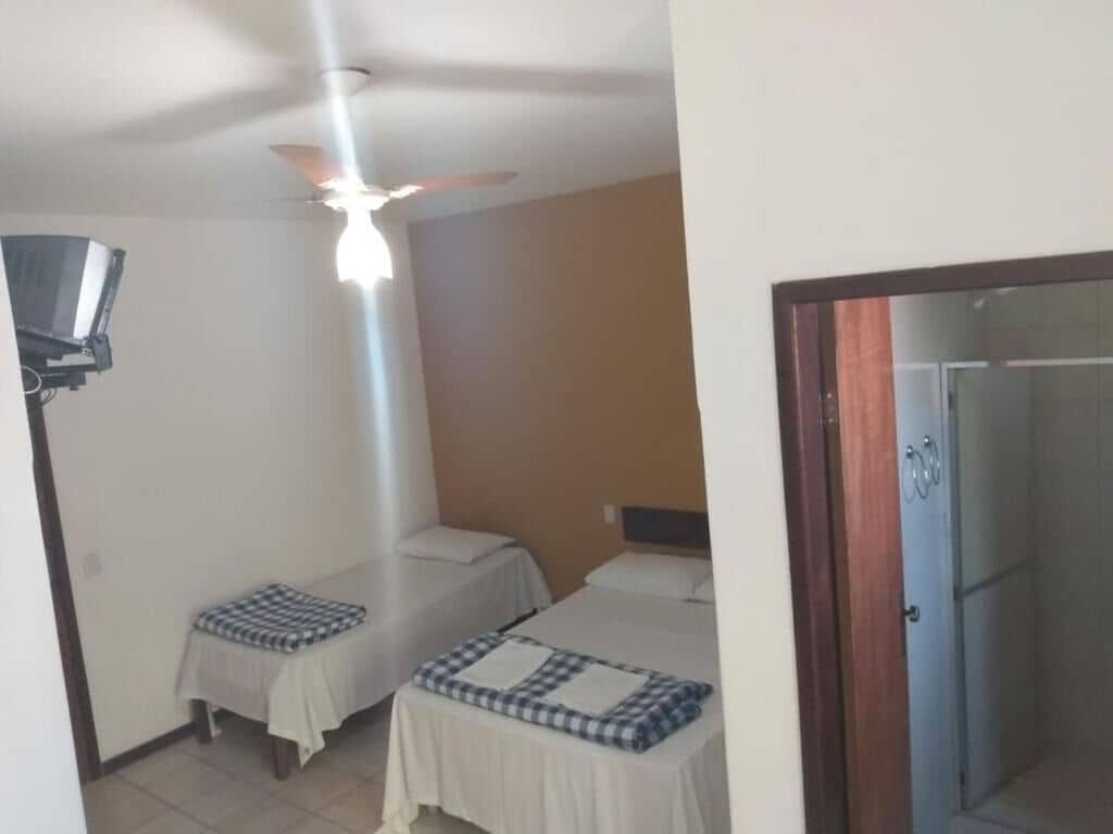 A room with two beds, a ceiling fan, and a shower area.