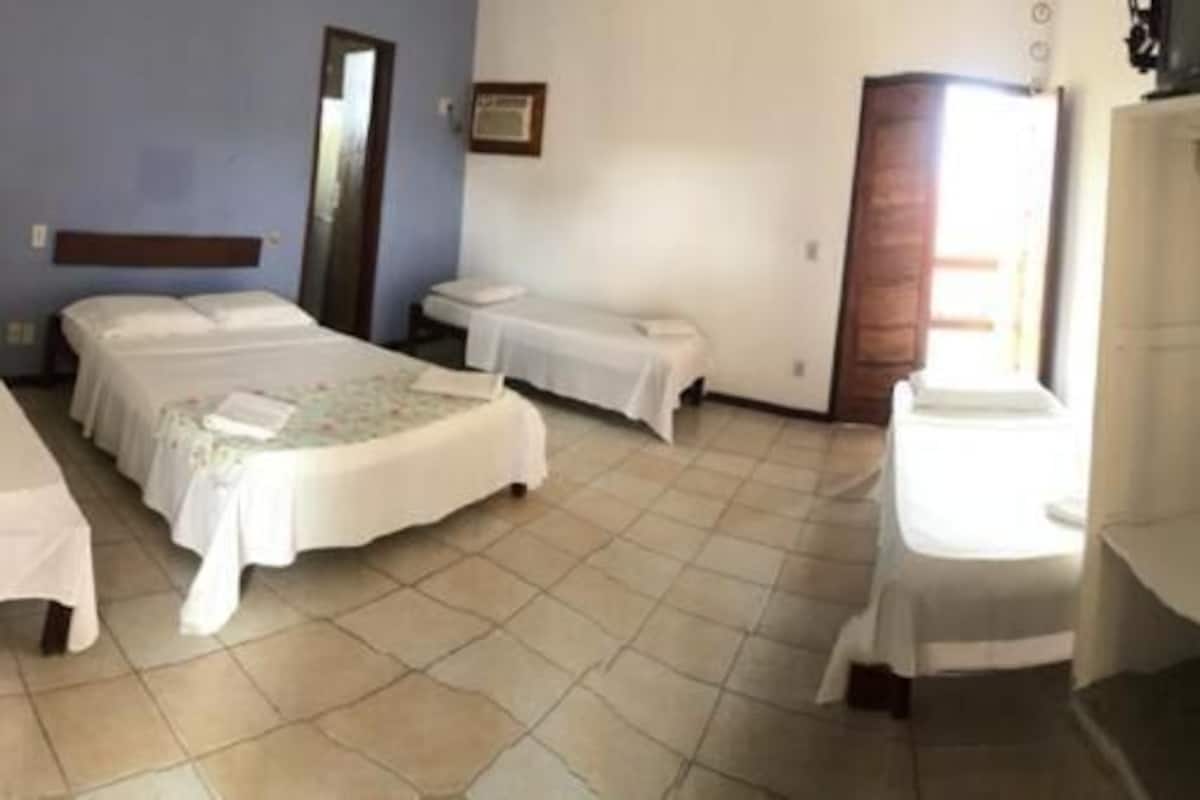 A hotel room with two beds, a small table, a wardrobe, and a shelf unit.