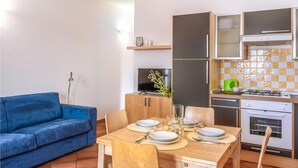 Un espacio habitable compacto con un sofá azul, una mesa de comedor para cuatro personas, un televisor, un refrigerador y una cocina con estufa y horno.