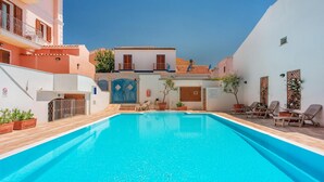 Una piscina con sillas de descanso y plantas en macetas, rodeada de edificios con balcones y puertas.