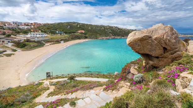 Un paisaje costero con una gran formación rocosa, aguas turquesas cristalinas y una playa de arena.