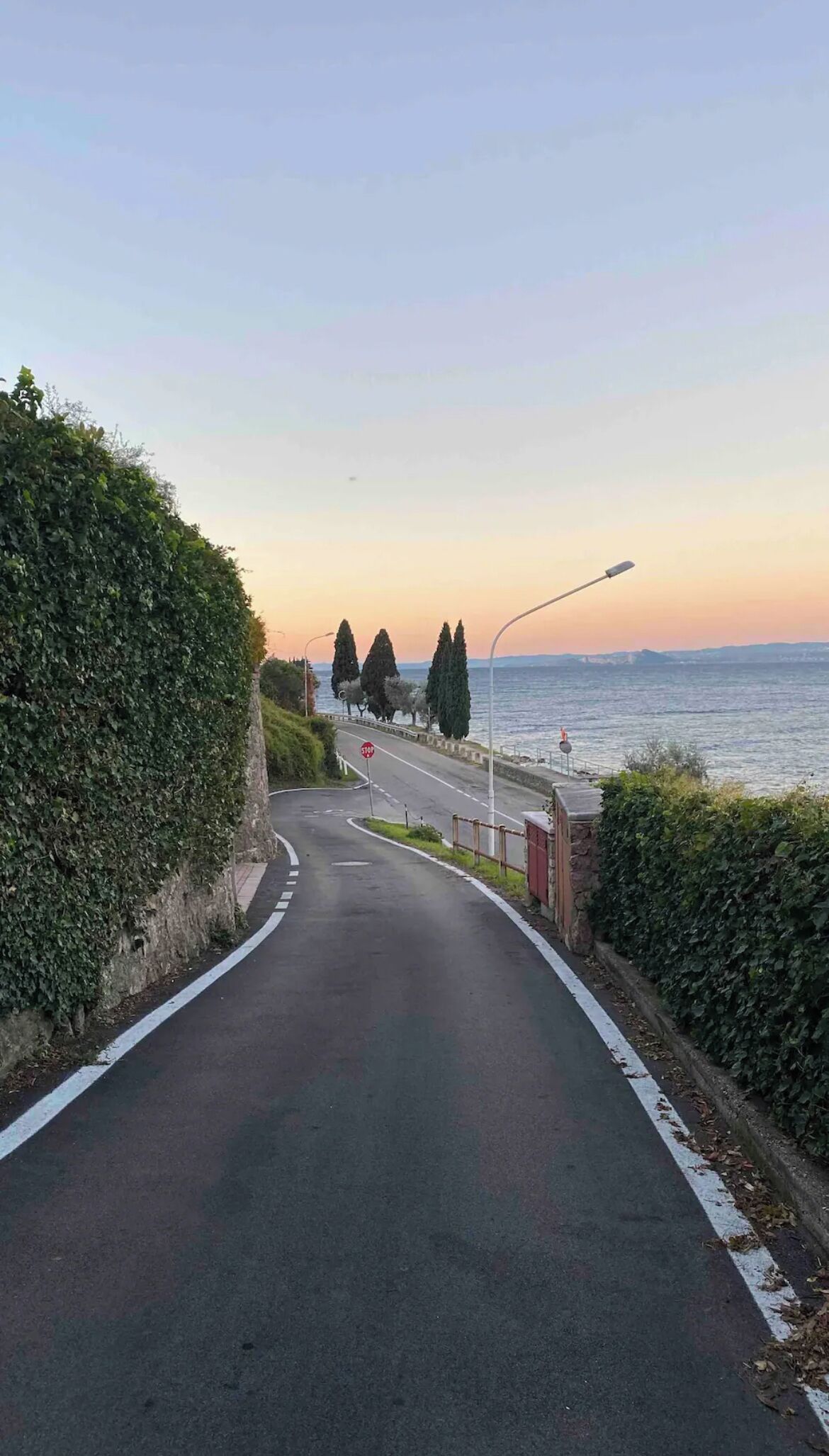 Una carretera costera con una señal de parada, un sendero peatonal y vistas al mar al atardecer.