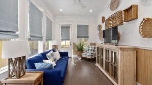 A spacious living room with a blue sofa, a wooden cabinet, and a television on a stand. - Gorgeous 4 bed/3.5 bath Home with Private Pool (St. Simons Island)