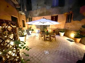 An outdoor patio with a table and chairs under a large umbrella, surrounded by potted plants and string lights. - NAVONA DOMITIA HOME LOFT LAWRENCE  (Roma)