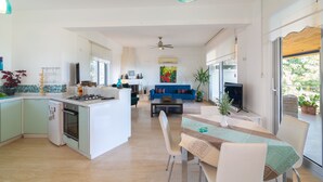A modern kitchen with a central island, a dining area with a table and chairs, a blue sofa, and a television.