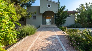 A modern building with a paved entrance, surrounded by lush greenery and a variety of plants.