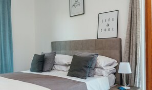 A neatly made bed with pillows, a bedside lamp, and two framed motivational quotes on the wall.