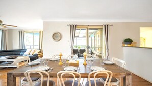 A dining area with a wooden table set for six, surrounded by white chairs. - WaterSide by Experience Jervis Bay (Sanctuary Point)