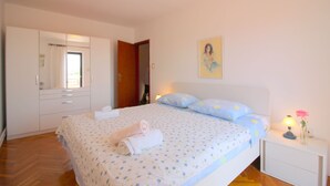 Ein Schlafzimmer mit Bett, Nachttisch mit Lampe, einem Gemälde an der Wand und einer Tür zu einem anderen Raum.
