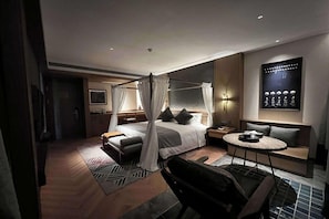 A modern hotel room with a four-poster bed, a sitting area with a round table, and a wall-mounted artwork. - Wyndham Fengqing Resort (Lincang)