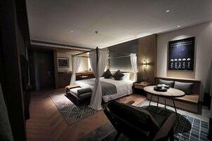 Una habitación de hotel moderna con una cama con dosel, una zona de estar con una mesa redonda y una obra de arte colgada en la pared.