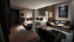 A modern hotel room with a four-poster bed, a sitting area with a round table, and a wall-mounted artwork. - Wyndham Fengqing Resort (Lincang)