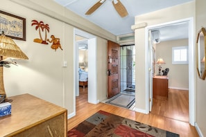 A hallway with a wooden floor, a patterned rug, a door with decorative panels, and a ceiling fan.