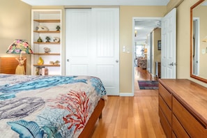 A bedroom with a bed, a dresser, a shelf with decorative items, and a door leading to another room.