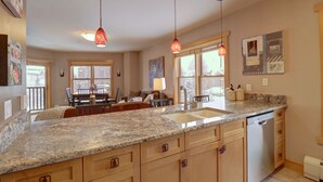 A kitchen with granite countertops, wooden cabinets, a dishwasher, pendant lights, and a dining area with a table and chairs. - Copper Springs Condo with Panoramic Mountain Views - CS331 by Redawning (Copper Mountain)
