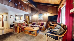 A cozy living room with wooden walls, a sofa, a coffee table, and a TV. - Horizons 4 186 Centrally Located, Spacious Mammoth Home with Cozy Fireplace by RedAwning (Mammoth Lakes)