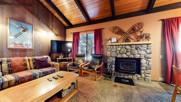 A cozy living room with a stone fireplace, leather chairs, a wooden coffee table, and a television. - Horizons 4 186 Centrally Located, Spacious Mammoth Home with Cozy Fireplace by RedAwning (Mammoth Lakes)