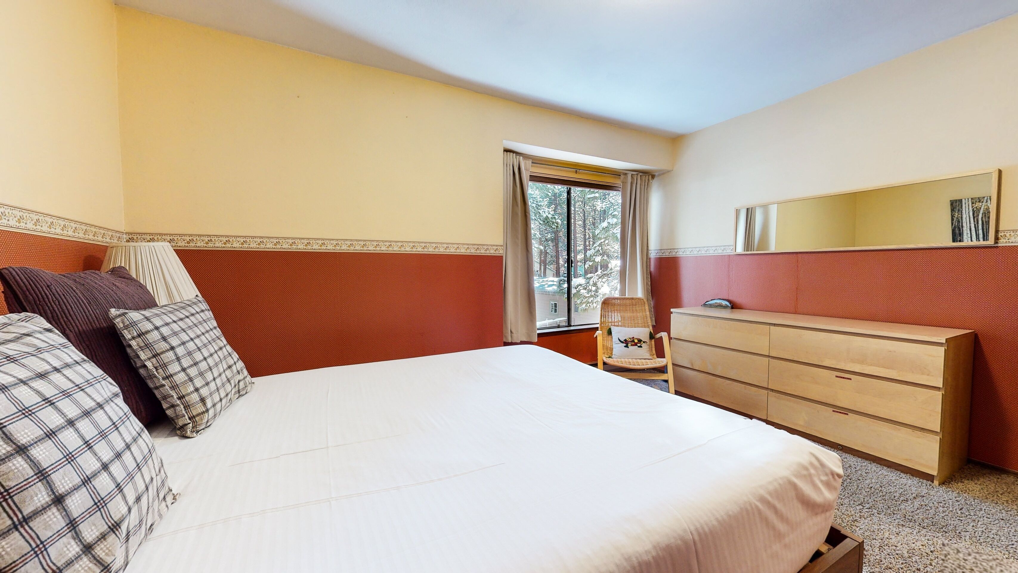Ett hotellrum med en stor säng, en byrå i trä, en stol och ett fönster med utsikt över träd.