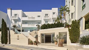 A modern hotel with a white facade, a staircase leading to the entrance, and potted plants around the building. - Oxygen Favie by GHH (Tinos)