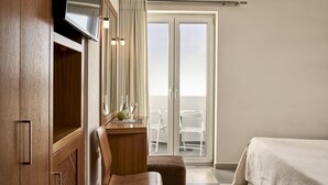 A hotel room with a wooden desk, a TV, a chair, a bed, and a balcony with a table and chairs. - Oxygen Favie by GHH (Tinos)