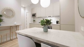 A modern kitchen with white cabinets, a marble countertop, and a central island with a vase of flowers. - San Martin - The Rentals Collection (San Sebastián)