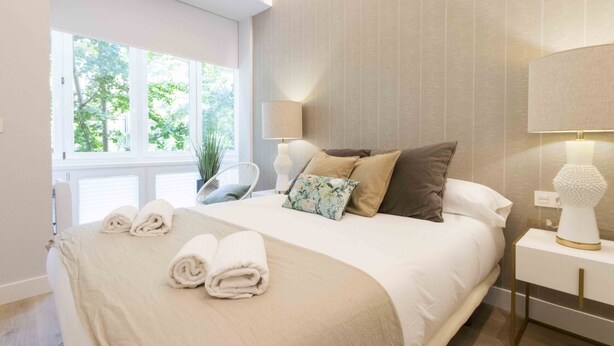 A neatly made bed with a beige bedspread, two pillows, and two rolled towels. - San Martin - The Rentals Collection (San Sebastián)