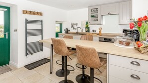 A modern kitchen with a central island, bar stools, and a built-in oven. - Pogles Wood Cottage (Skipton)