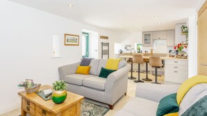 A modern living room with a grey sofa, wooden coffee table, and a kitchen in the background. - Pogles Wood Cottage (Skipton)