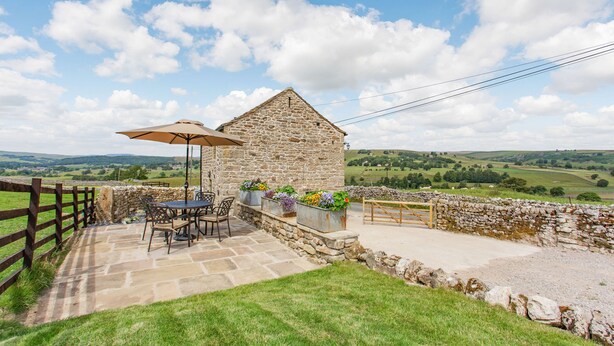 A stone building with a patio area, outdoor seating, and flower planters. - Pogles Wood Cottage (Skipton)