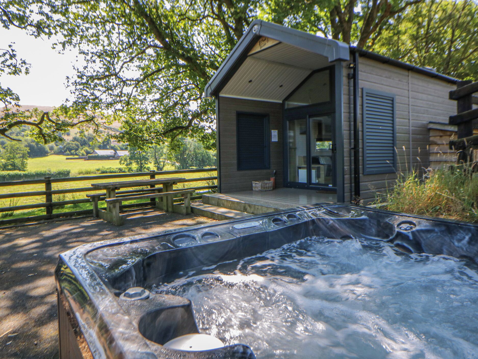 A hot tub with a wooden deck, a wooden cabin with a glass door, and a wooden fence.