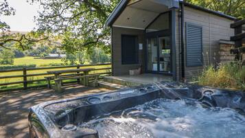 Ein Whirlpool mit Holzterrasse, eine Holzhütte mit Glastür und ein Holzzaun.