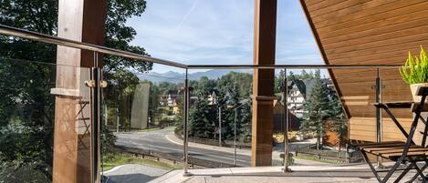 A balcony with a glass railing, a potted plant, and a view of a road and buildings.