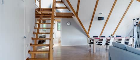 A spacious loft with a wooden staircase, a dining area, and a living room with a sofa.