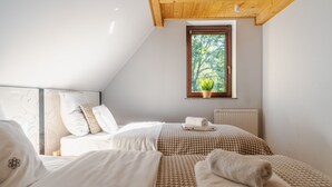 Un dormitorio con dos camas, una ventana con vistas a árboles, un radiador y una planta en maceta.