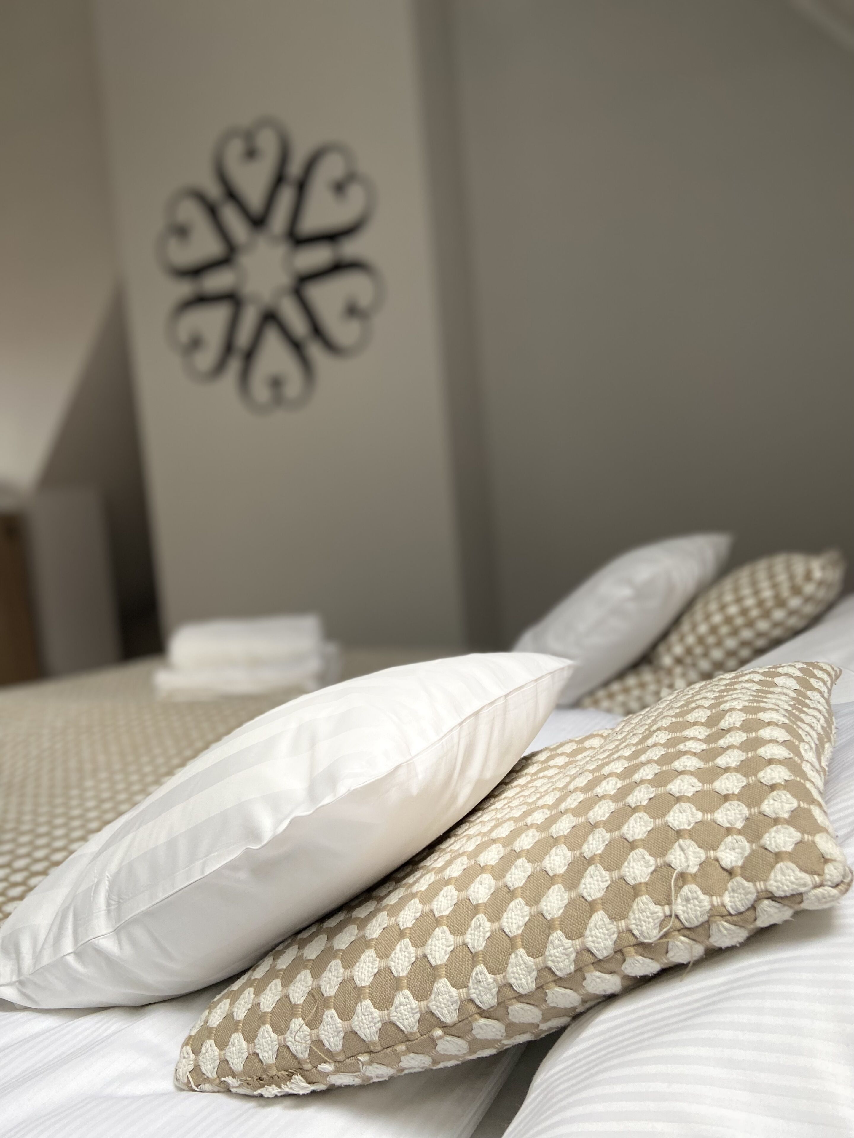 A neatly made bed with white and beige patterned pillows, a decorative wall piece, and a stack of white towels.