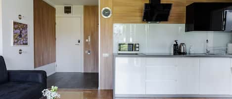 A modern kitchen with white cabinets, a microwave, and a coffee maker. There is a black sofa and a glass table with a vase of flowers.