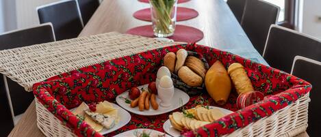 Una mesa de comedor con una bandeja de mimbre que contiene diversos alimentos, un florero con flores y una camino de mesa roja.