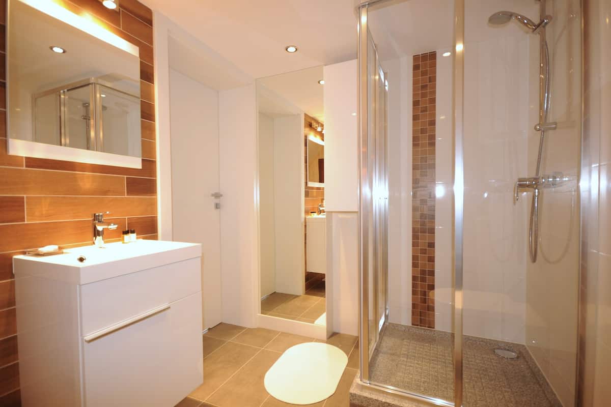Un baño moderno con cabina de ducha de vidrio, tocador blanco con espejo y piso de baldosas.