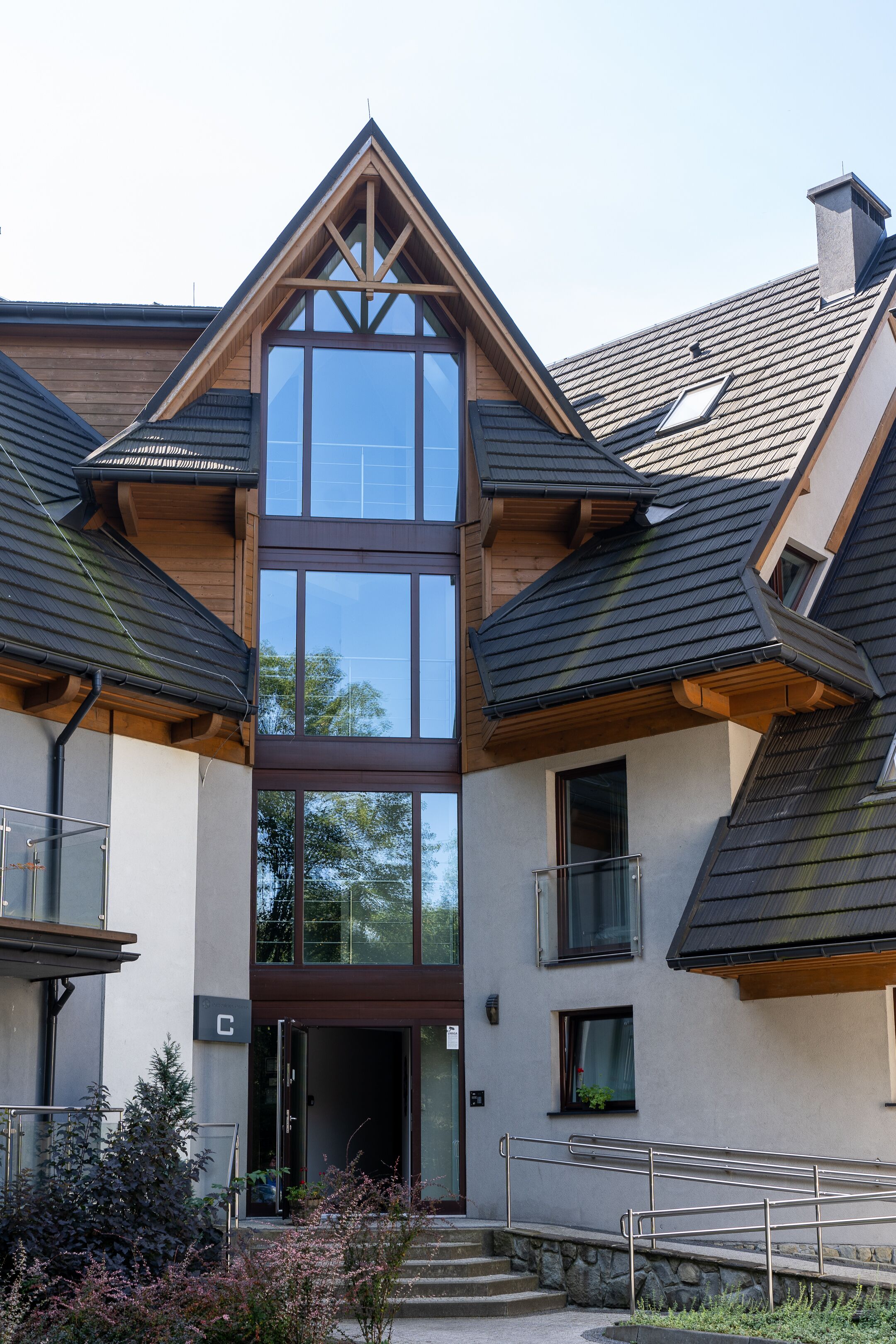 A modern building with a central glass tower, wooden balconies, and a stone staircase leading to the entrance.