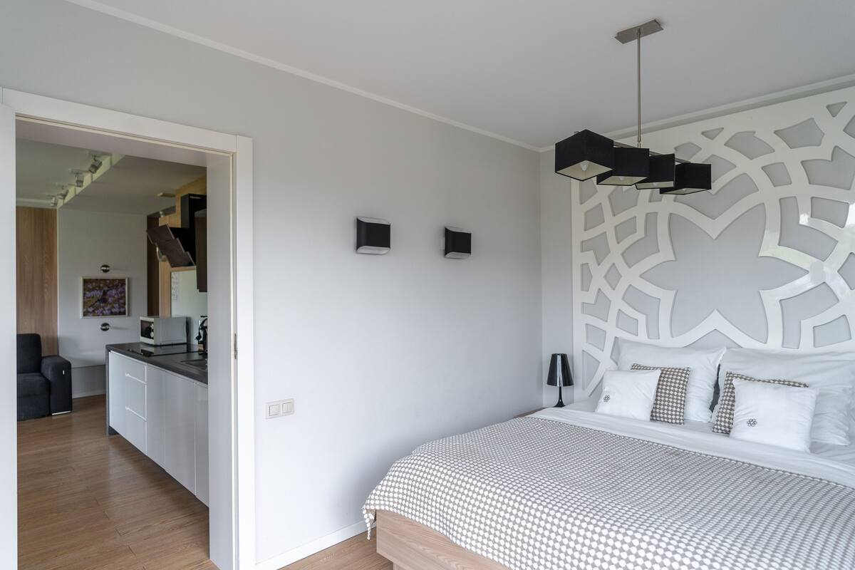 Un dormitorio con cama, mesita de noche, lámpara y un panel decorativo en la pared.