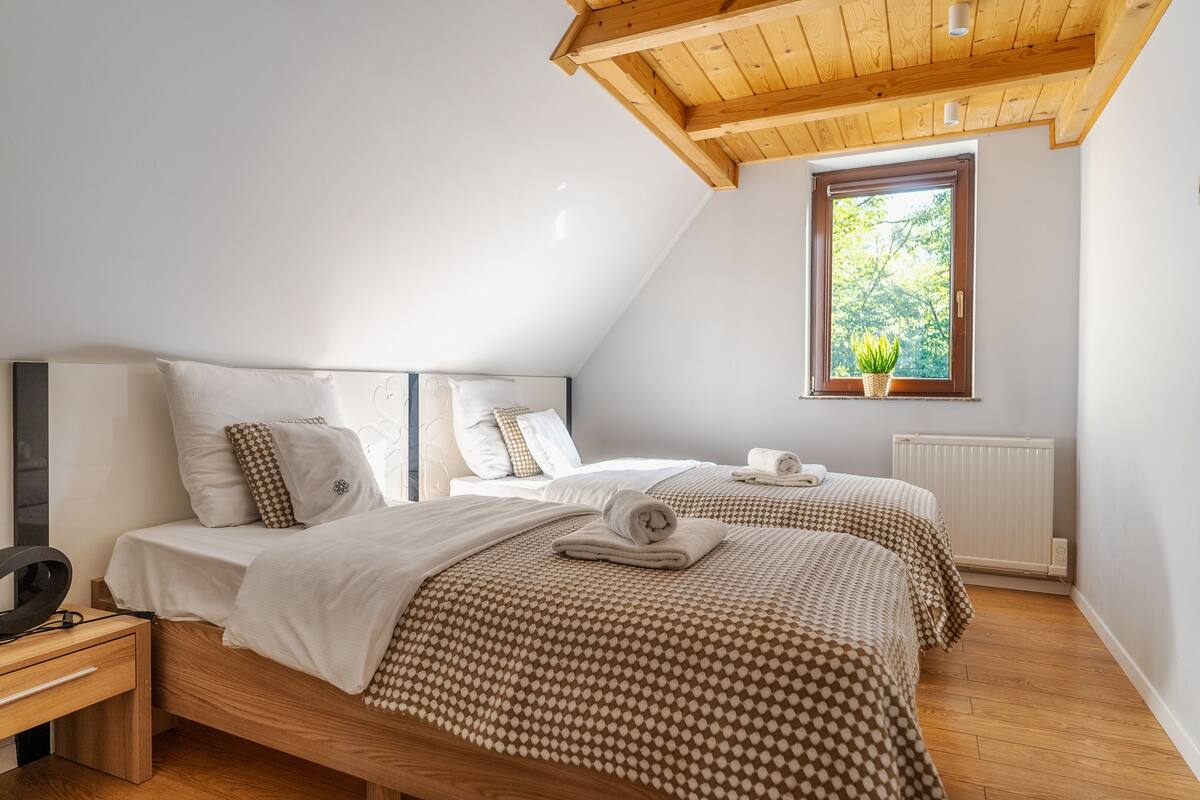 Un dormitorio con dos camas, cabeceros de madera, una ventana con vistas a árboles y un radiador.