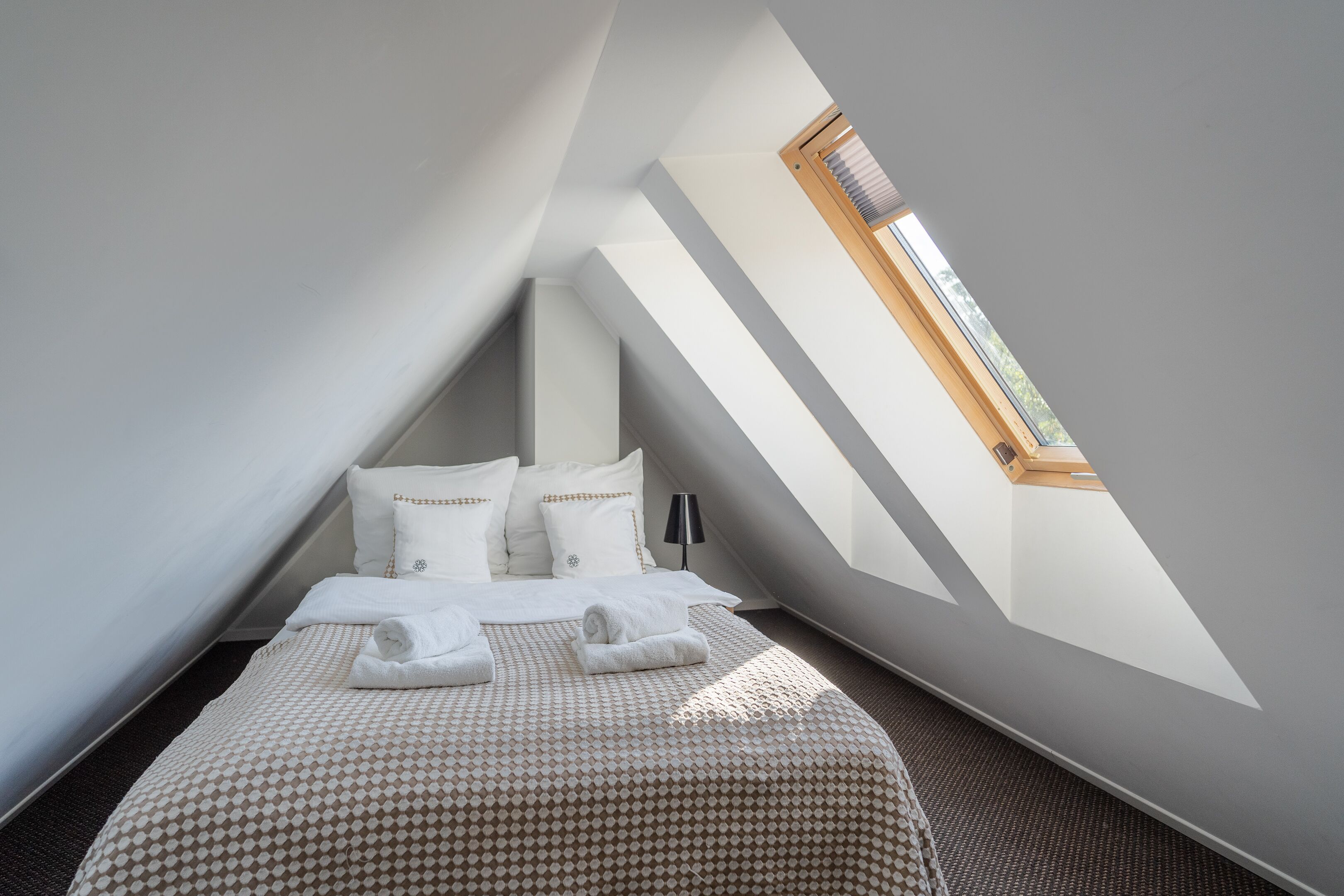 A bedroom with a sloped ceiling, a skylight, a bed with white linens, and a patterned bedspread.