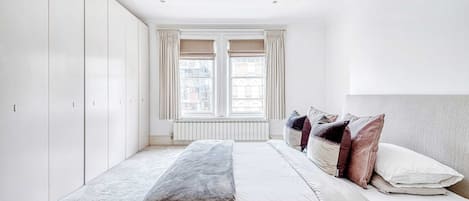 A bedroom with a bed, a radiator, and a window with curtains.