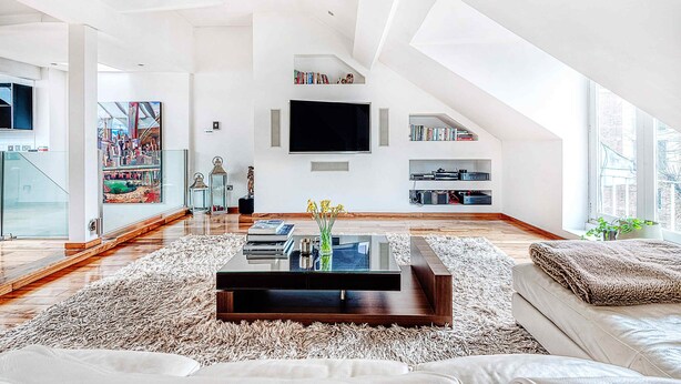 A spacious living room with a large flat-screen TV, a coffee table, and a bookshelf.